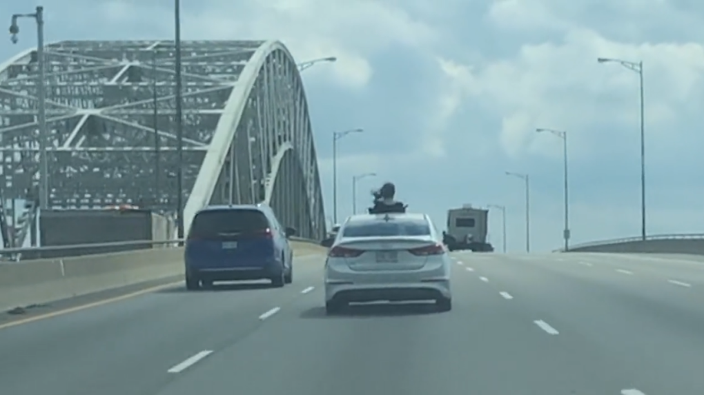 Video released by the Ontario Provincial Police (OPP) shows a car passenger hanging out of the vehicle’s sunroof as it crosses what appears to be the Burlington Skyway bridge on the QEW west of Toronto. (OPP via Twitter) 
