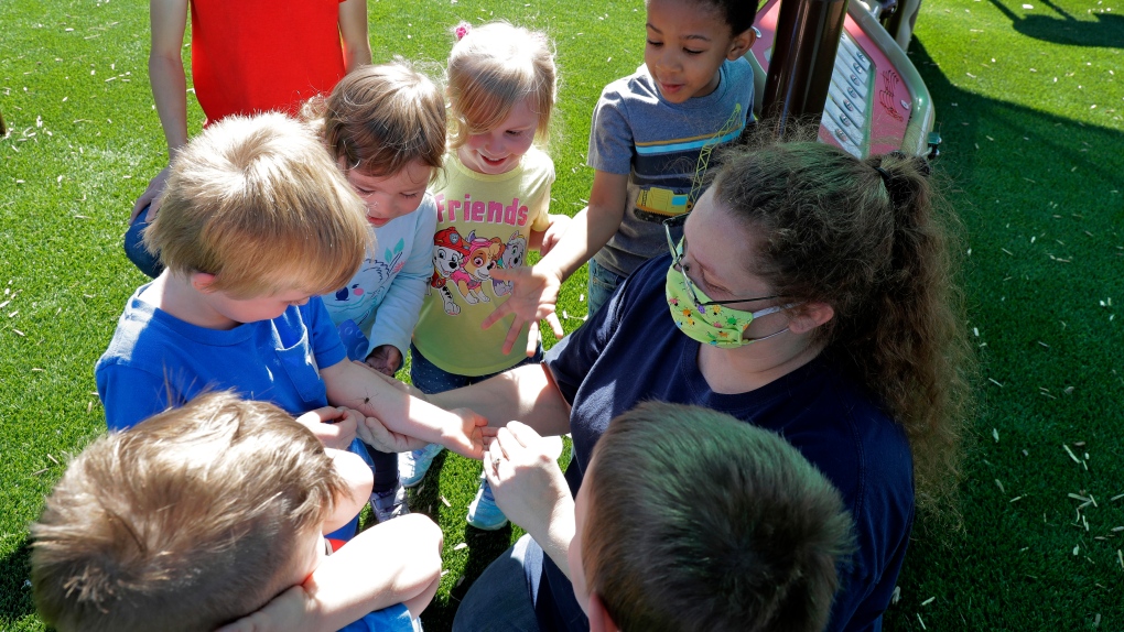 In this May 27, 2020 photo, teachers Jana Blair, right, and Aaron Rainboth, upper left, wear masks as they work with kids examining a spider they found on the playground at the Frederickson KinderCare daycare center, in Tacoma, Wash. (AP Photo/Ted S. Warren)