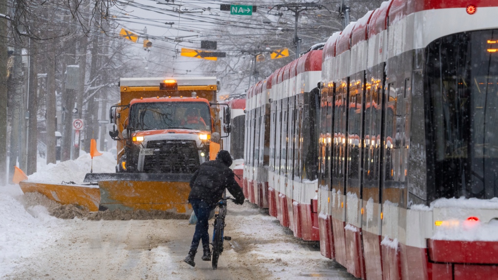 A cyclict hops off his bike to get out of the way of a snow plow while making his way past dozens of stranded streetcars during a severe winter storm in Toronto on Monday January 17, 2022. THE CANADIAN PRESS/Frank Gunn