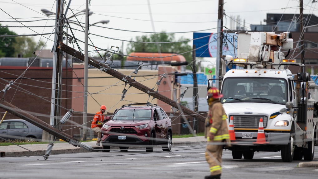 A utility worker speaks to a motorist remaining in their vehicle, as crews work to make sure they can leaves safely, after power lines and utility poles came down onto the roadway during a major storm, on Merivale Road in Ottawa, on Saturday, May 21, 2022. (Justin Tang/THE CANADIAN PRESS)